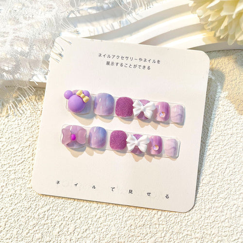 Lavender-hued kids press-on nails with purple glitter and floral embellishments on display card