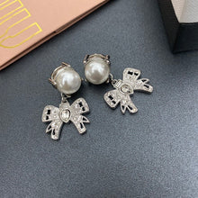 Cargar imagen en el visor de la galería, Pendientes en tono platino con lindos y elegantes lazos adornados con perlas de resina de gran tamaño y cristales blancos.
